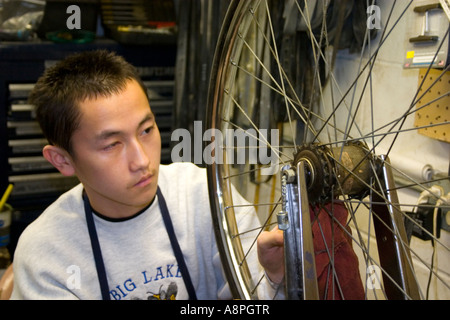 Asian American worker making a bike wheel repair. Youth Express Bike Shop St Paul Minnesota USA Stock Photo