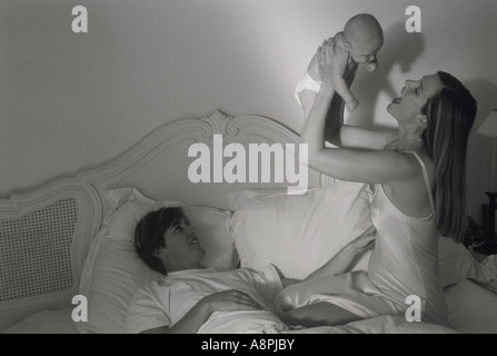 Mother holding baby overhead in bed above proud father Stock Photo