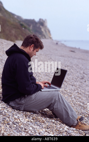 man beach laptop wireless work relax pebble devon Stock Photo