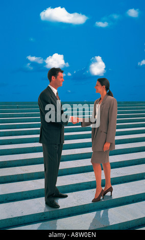 Montage concept of man and woman shaking hands whilst standing on steps against blue sky. Stock Photo