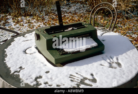 old IBM typewriter covered with snow standing on a garden table with two hand prints in front of it Stock Photo