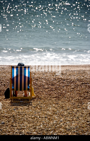 Person sitting in a backlit deckchair on the beach at Eastbourne, Sussex, England, UK Stock Photo