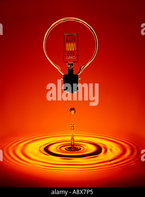 GLASS ELECTRIC LIGHT BULB WITH GLOWING FILAMENT FLOATING ABOVE POOL OF AMBER WATER WITH RIPPLES Stock Photo