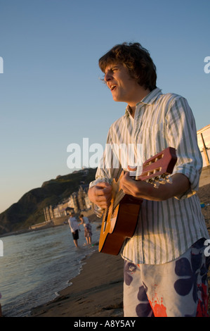 seaside Aberystwyth wales one man strumming guitar and singing songs at sunset summer evening - university student, wales UK Stock Photo