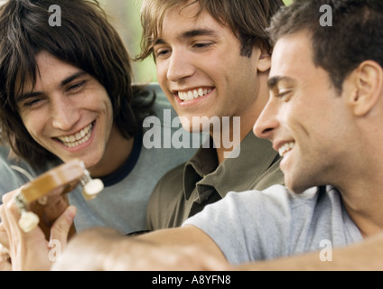 Three young male friends, looking at guitar Stock Photo