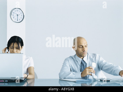 Office, man holding telephone while woman uses computer Stock Photo