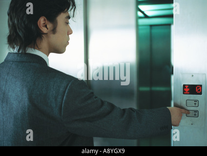 Young man in suit pushing button for elevator Stock Photo