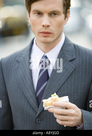 Young businessman holding half-eaten sandwich Stock Photo