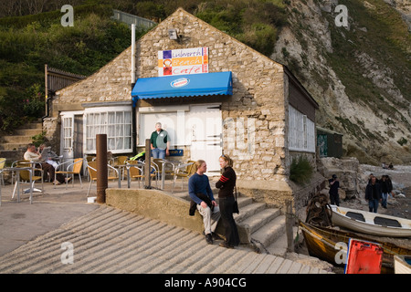 Slipway for boat launching and tourist couple outside Lulworth Cove beach cafe Dorset UK Stock Photo