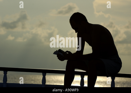 Silhouette of a man on holiday reading a book overlooking the ocean Stock Photo