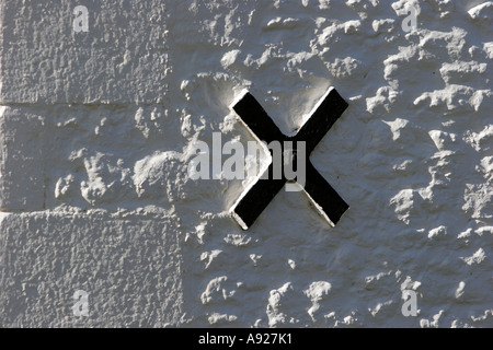Black cross shaped brace on exterior of limewashed stone wall Stock Photo