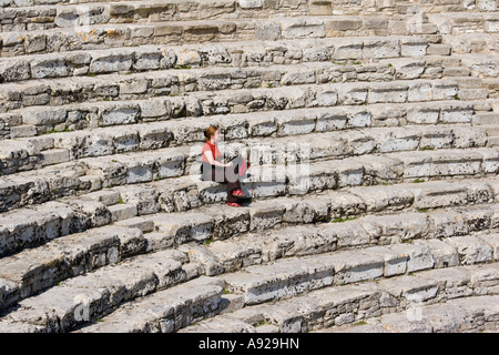 Woman sitting alone on stone seats in the 5th Century BC Greek theater Segesta Sicily Italy Stock Photo