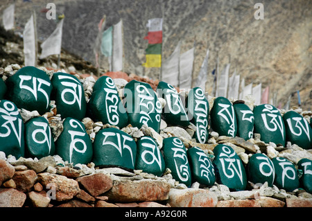 Tibetan script on green painted stones set in a row in front of prayer flags at monastery Tashi Gompa Phu Nar-Phu Annapurna Reg Stock Photo