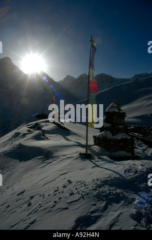Bright rays of the sun on a prayer flag and choerten in the snow-capped high mountains near Thorung La Pass Annapurna Region Ne Stock Photo