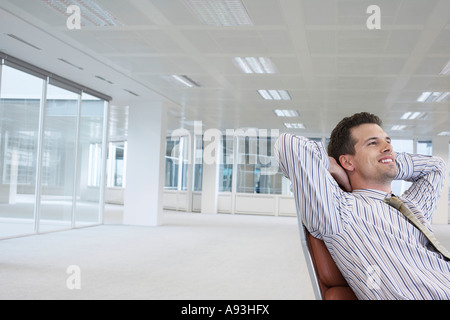 Office worker leaning back in swivel chair, hands behind head, in empty office space Stock Photo