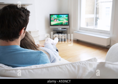 Father and daughter (5-6) watching cartoons in television, back view Stock Photo