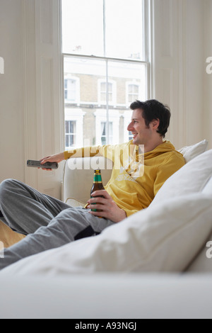 Man sitting on sofa, watching television and holding beer bottle Stock Photo