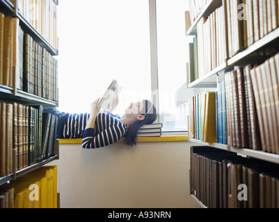 Student lying down on windowsill in library reading Stock Photo