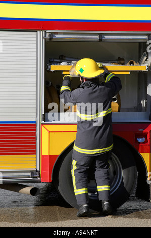 firefighter in protective clothing reaches into fire engine for equipment during incident Stock Photo