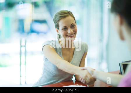 Two women shaking hands across counter Stock Photo