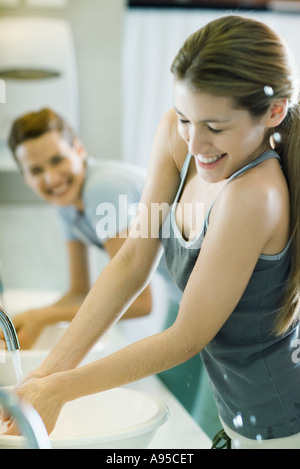 Two women washing hands in sinks, one getting splashed Stock Photo