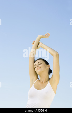 Woman stretching arms overhead, sky in background, low angle view Stock Photo