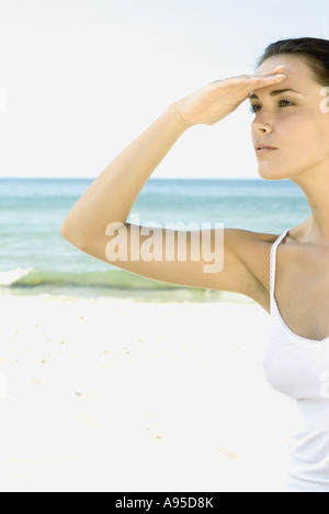 Woman shading eyes, looking away beach in background Stock Photo