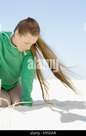 Woman with long hair kneeling on sand Stock Photo