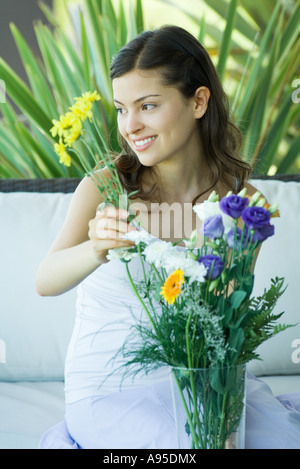 Young woman making flower arrangement, looking away, smiling Stock Photo