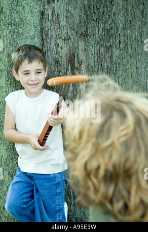 Boy holding hot dog on end of large fork, showing friend Stock Photo