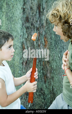 Boy holding hot dog on end of large fork, showing friend Stock Photo