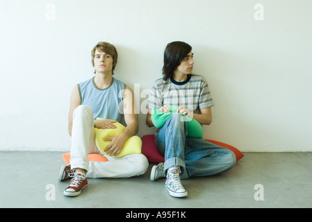 Teenage friends sitting on cushions on floor, full length Stock Photo