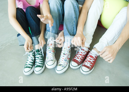Friends sitting on floor, wearing canvas shoes, tying laces, low section Stock Photo