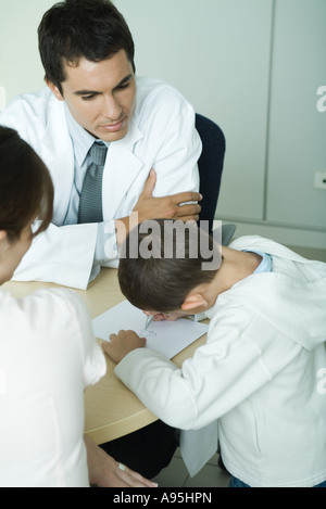 Doctor sitting with boy and woman, boy drawing on paper, high angle view Stock Photo