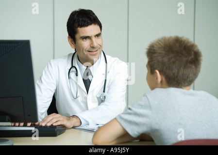 Doctor sitting across from boy, using computer, smiling at boy Stock Photo