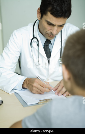 Doctor sitting across from boy, writing on clipboard Stock Photo