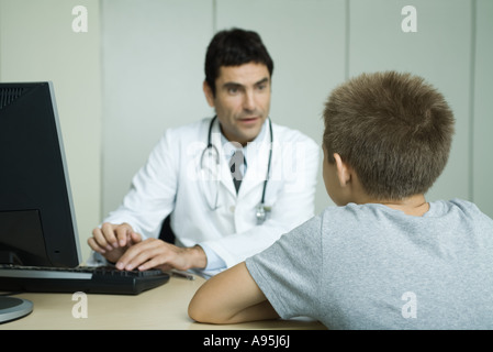 Doctor sitting across from boy, using computer Stock Photo