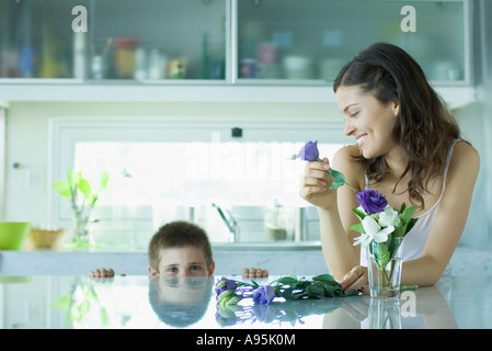 Young woman making fresh flower arrangement, smiling at boy Stock Photo