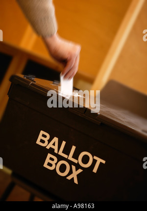 WHITE MALE HAND PLACING VOTE IN BALLOT BOX AT POLLING STATION Stock Photo