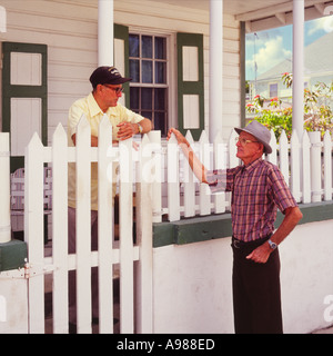 Local elderly man talks to another island inhabitant over his white garden fence at Green Turtle Cay Abaco Island The Bahamas Stock Photo