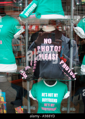 Funky T Shirts in a London Shop window with clear reflection of photographer holding camera with words on shirt England Stock Photo