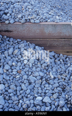 Detail of coastal timber groyne with tons of smooth grey pebbles banked unevenly against it through power of tides Stock Photo