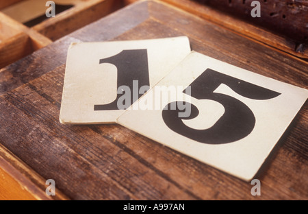 Old-fashioned numerals 1 and 5 printed in black on individual square white cards lying in warm light on lid of hymn numbers box Stock Photo