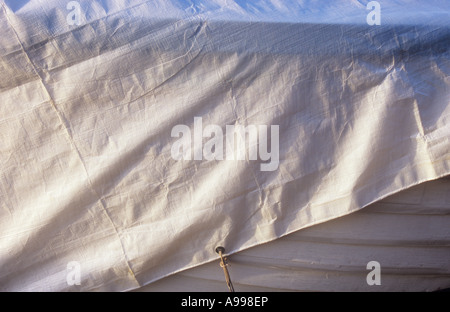 Detail of white plastic-coated tarpaulin sheet covering white painted timber boat casting shadows in warm light Stock Photo