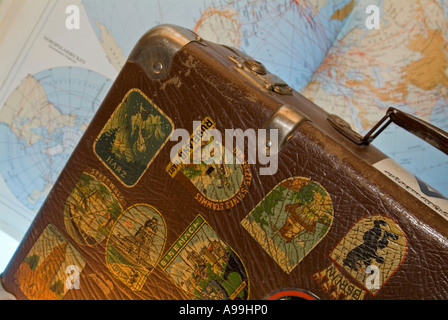 old suitcase with many stickers as souvenirs from different towns in front of a world map Stock Photo