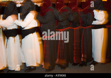 Hooded members of a religious fraternity wearing robes carry a float ...