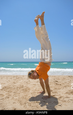 Smiling man doing handstand on beach Stock Photo