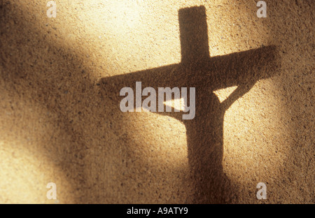 A shadow against a pale rendered wall of Jesus Christ hanging from a crucifix with other shadows of windows or archway Stock Photo