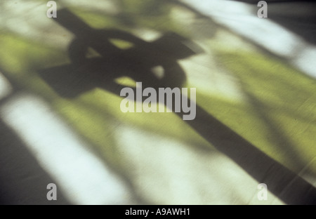 Shadow of a Celtic cross crucifix cast onto a pale background with the projection of a green and plain leaded church window Stock Photo