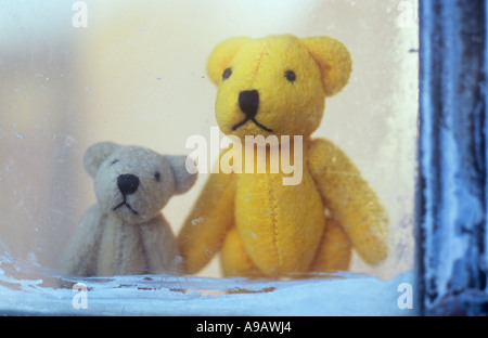 Close up of a mum or dad or sibling teddy bear with a young child ted standing looking out yearningly through a window Stock Photo